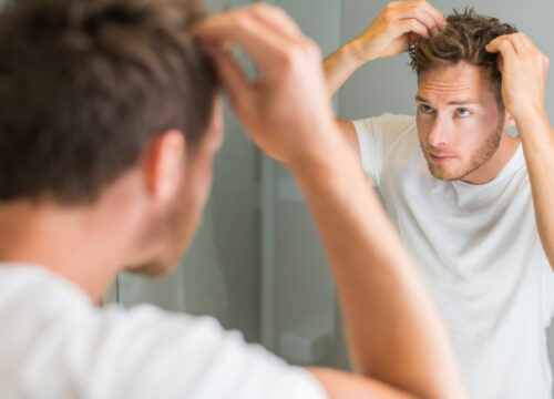 Man with a full head of hair checking out his hairline in the mirror